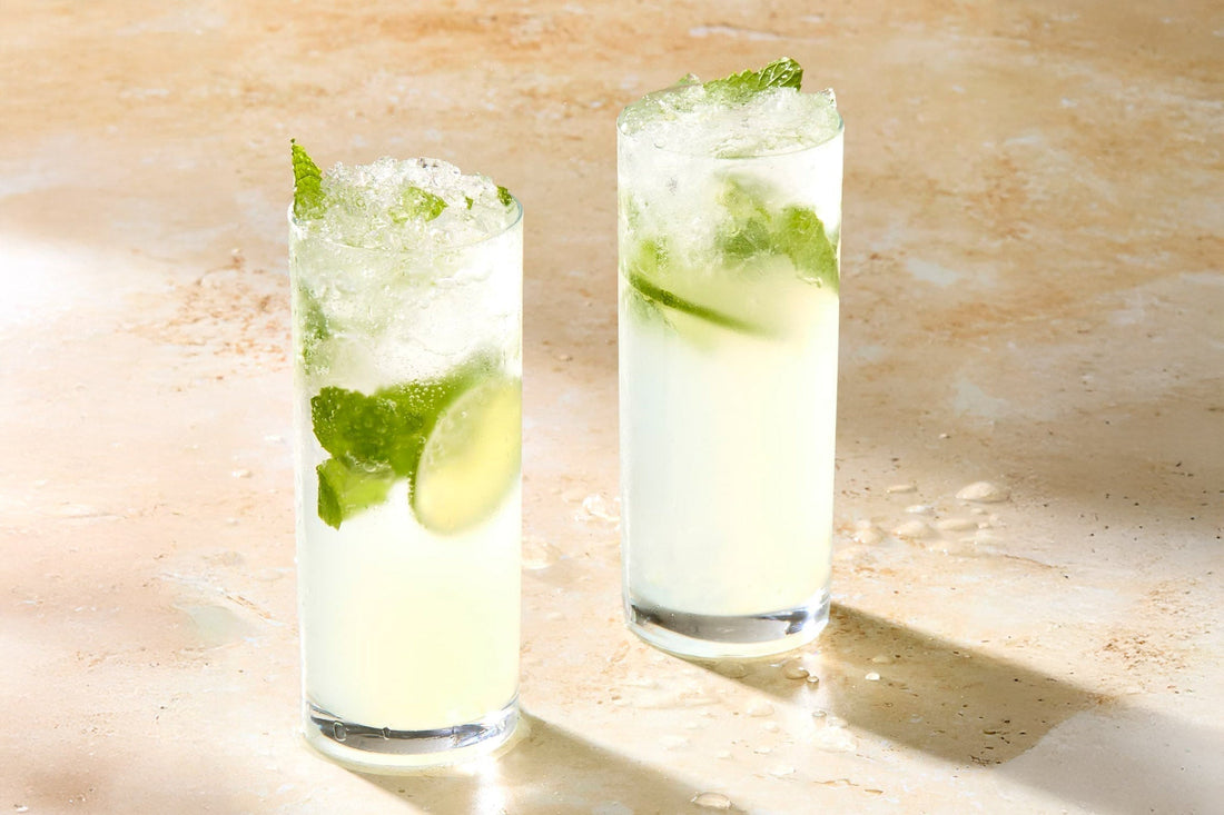 Two tall glasses of the Mojito cocktail on a countertop