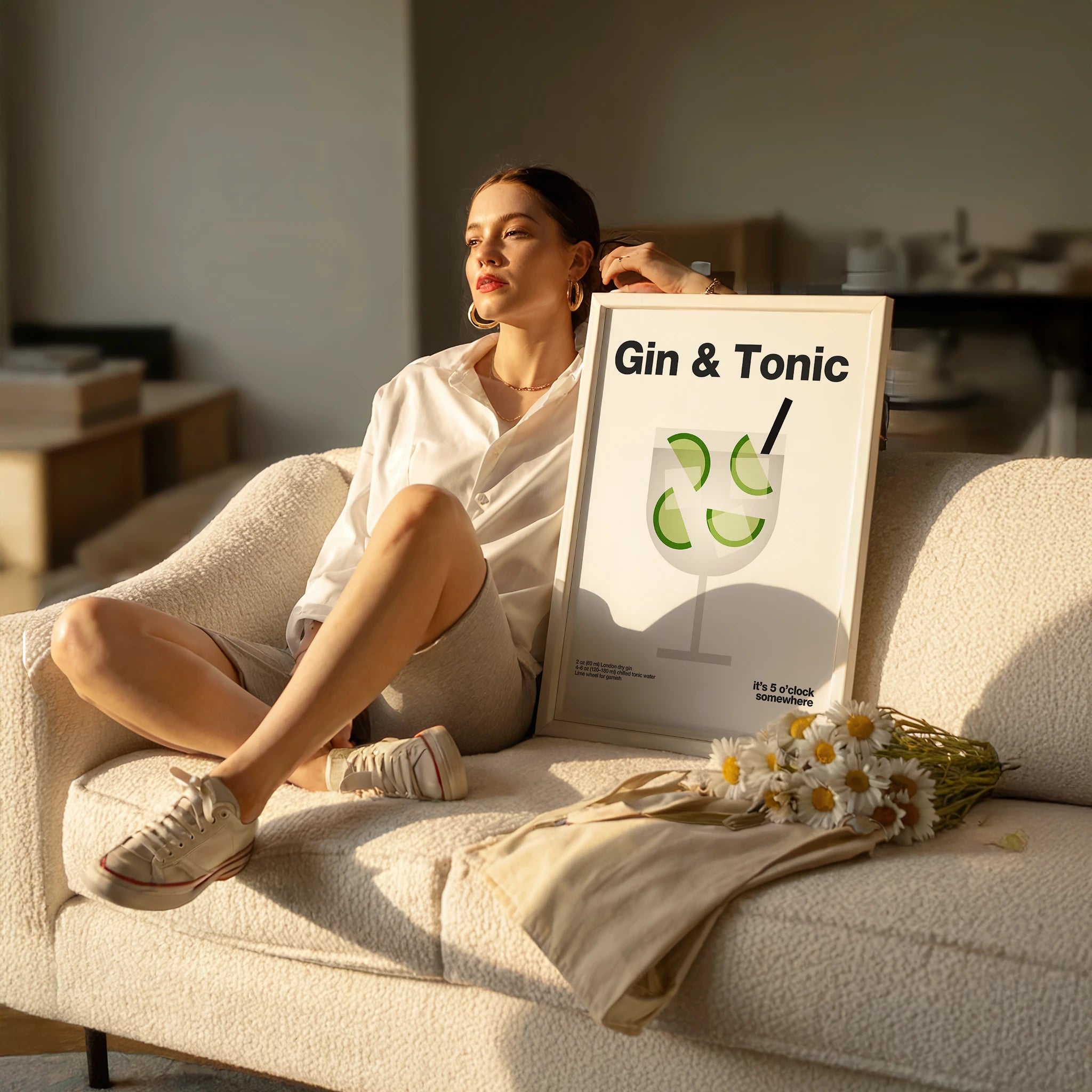 Woman sitting on a couch with a 'Gin & Tonic' sign and flowers in a bright room