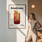 Woman standing next to a framed poster with 'Americano' design in a room with soft lighting.