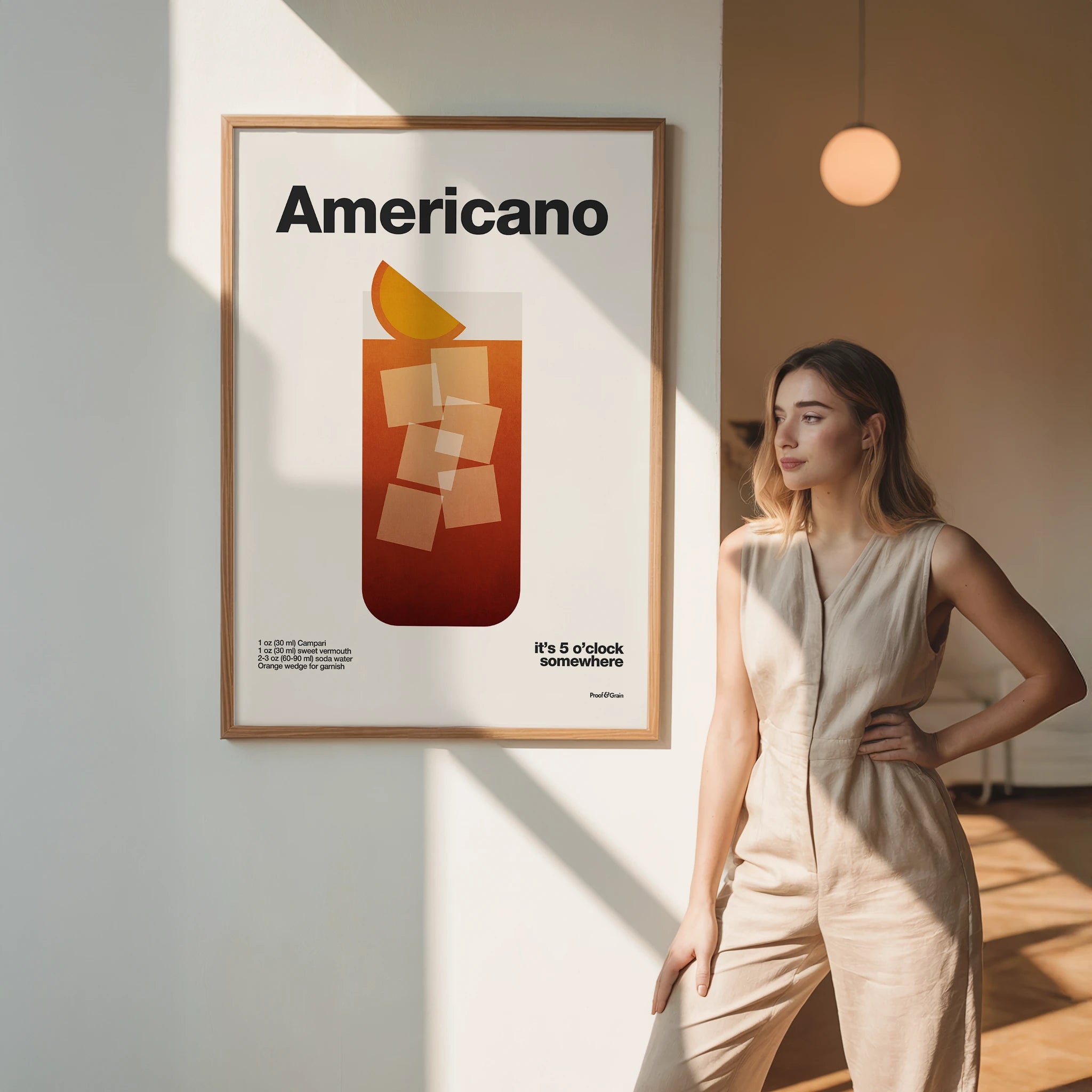 Woman standing next to a framed poster with 'Americano' design in a room with soft lighting.