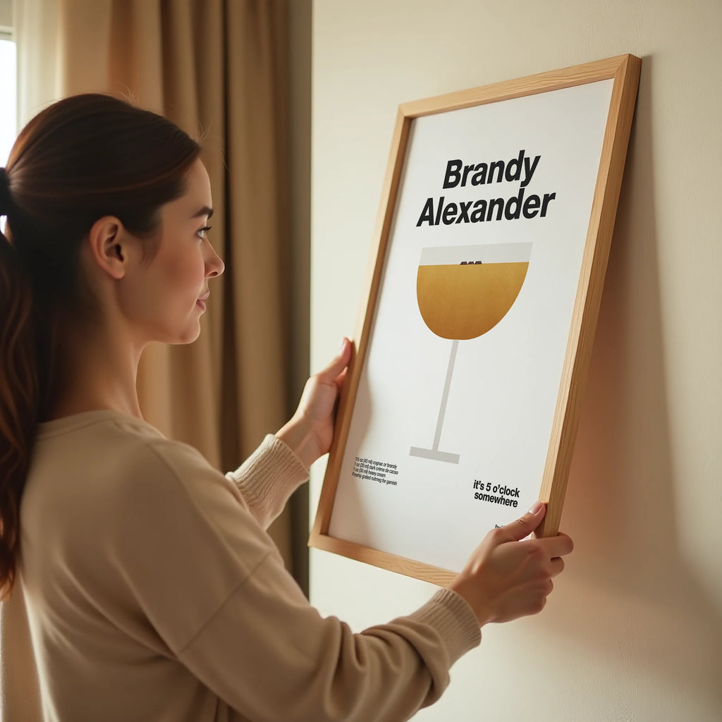 Woman holding a framed poster with 'Brandy Alexander' recipe on a wall.