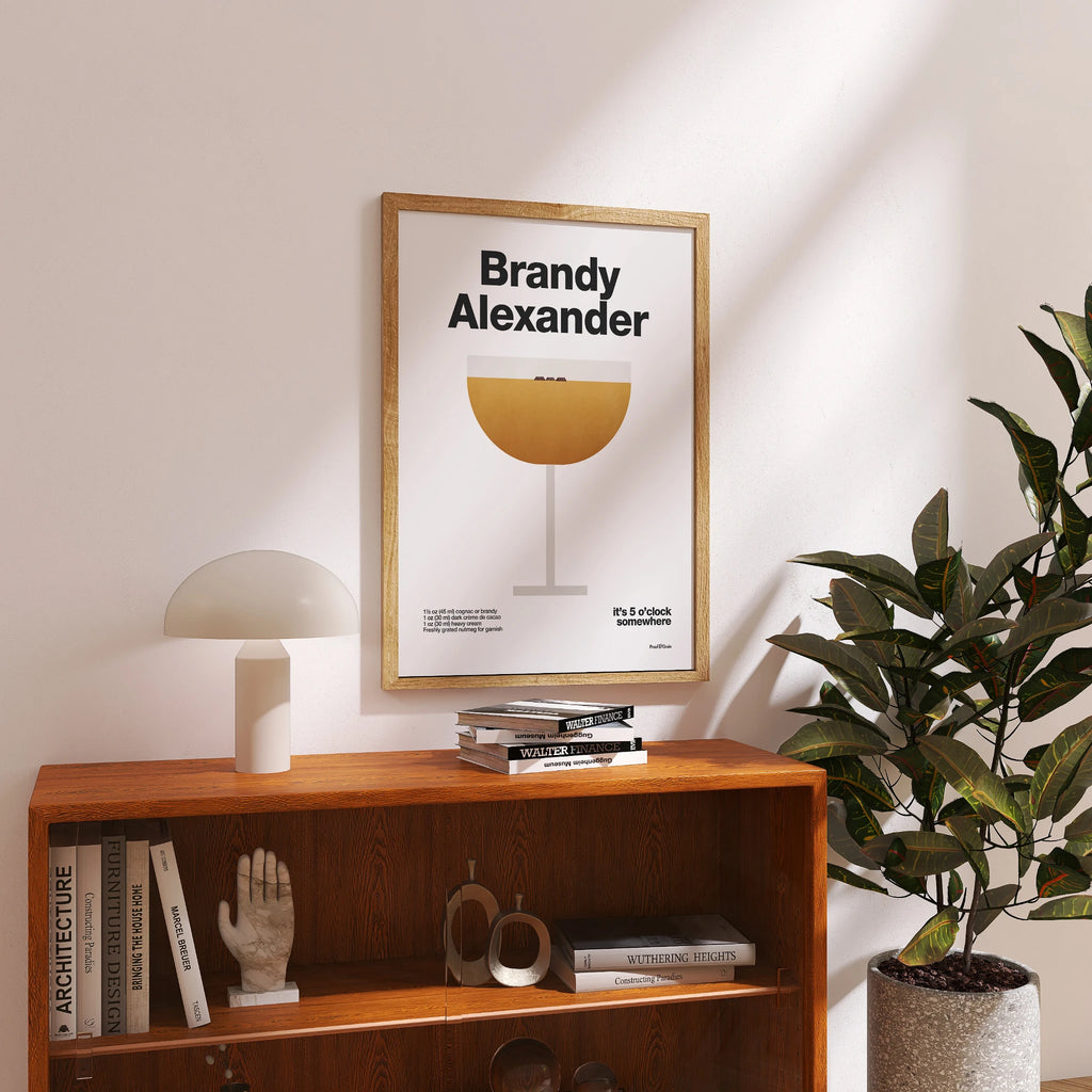 Framed poster titled 'Brandy Alexander' on a wooden shelf with books and decor.