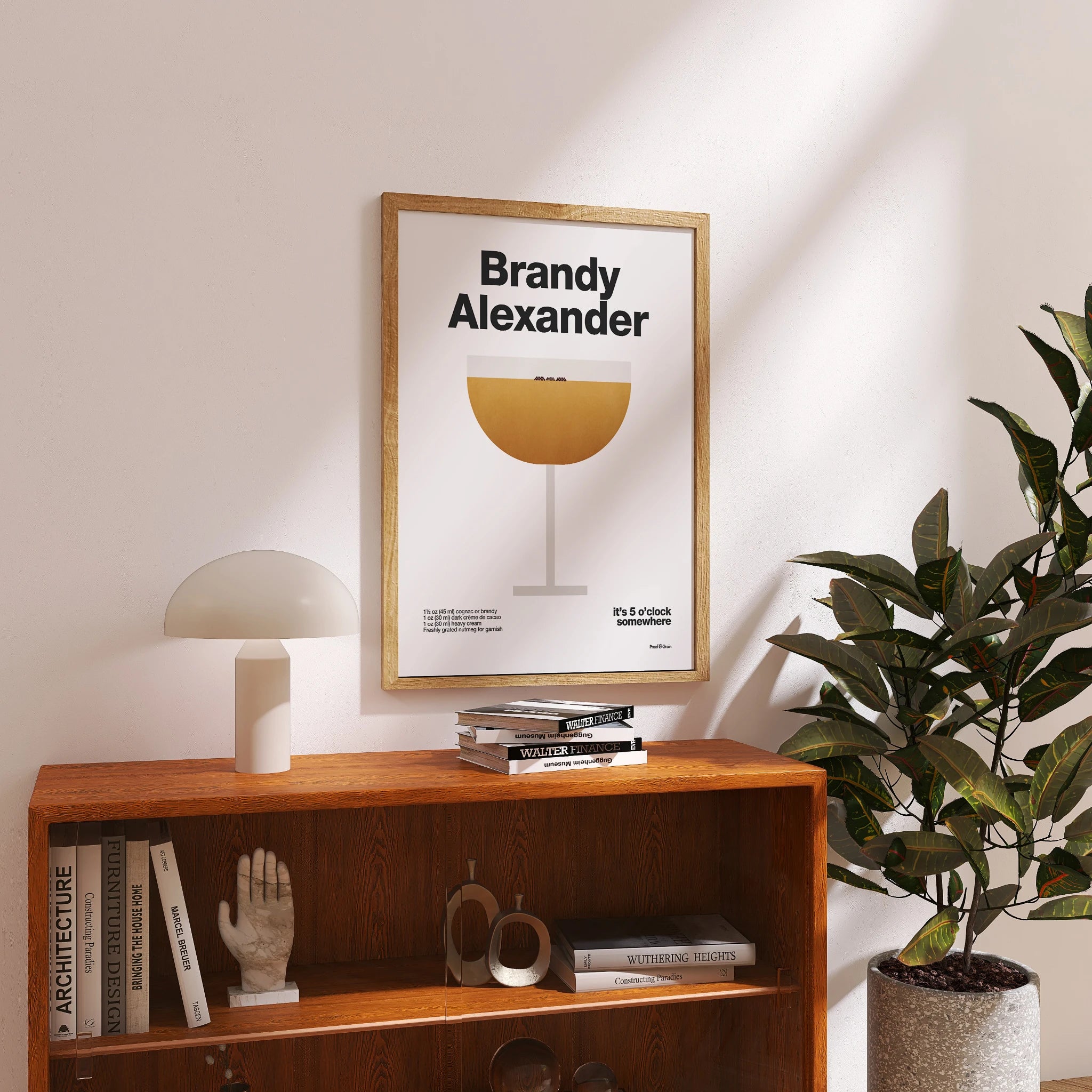 Framed poster titled 'Brandy Alexander' on a wooden shelf with books and decor.