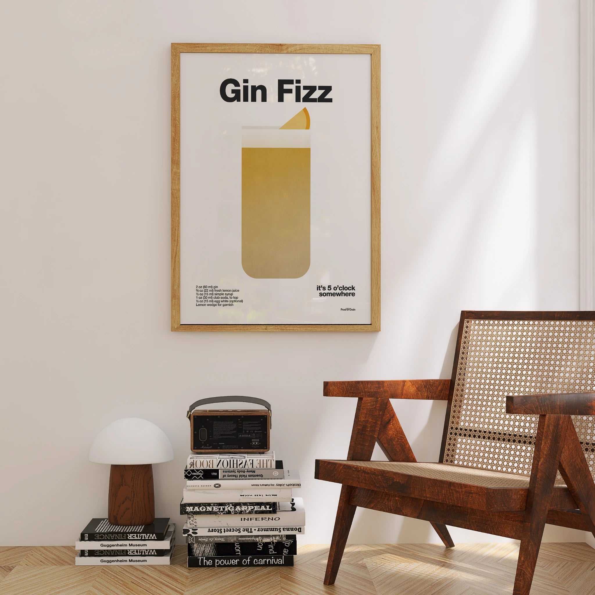 Framed poster with 'Gin Fizz' design on a wall above books, next to a wooden chair.