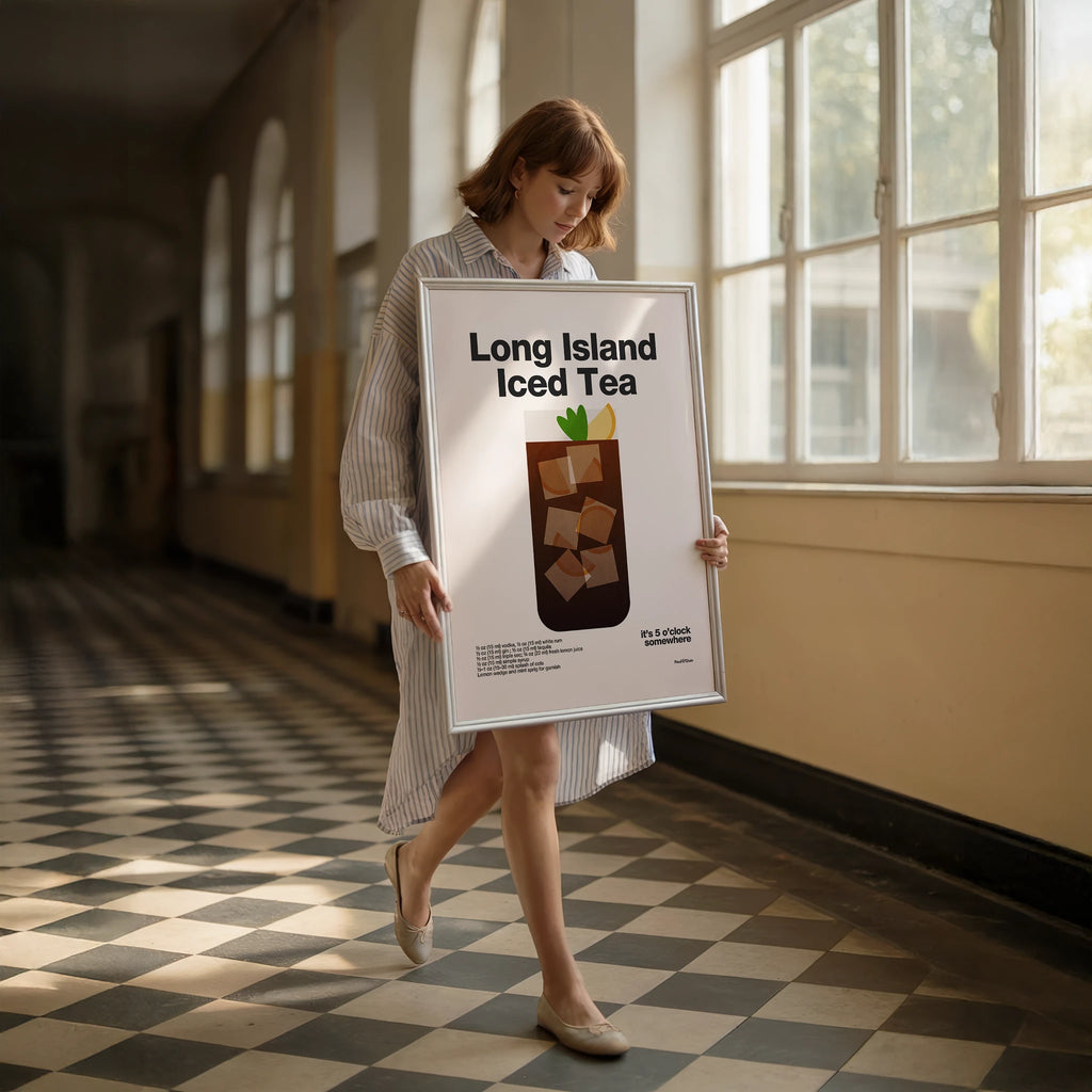 Woman holding a framed picture titled 'Long Island Iced Tea' in a sunlit room.