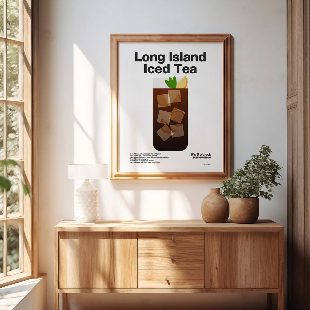 Framed poster of a Long Island Iced Tea on a wall above a wooden cabinet with plants.