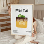 Person holding a framed poster with 'Mai Tai' design and text in a bedroom setting.