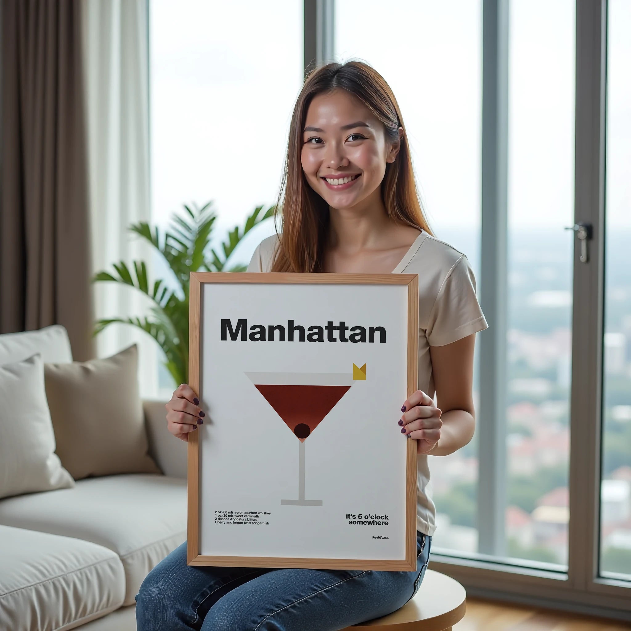 Woman holding a framed poster with 'Manhattan' cocktail design in a living room.