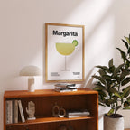 Framed 'Margarita' poster on a shelf with books and decor