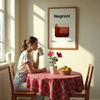 Woman sitting at a table with a red checkered tablecloth, drinking from a mug, with a 'Negroni' poster on the wall.