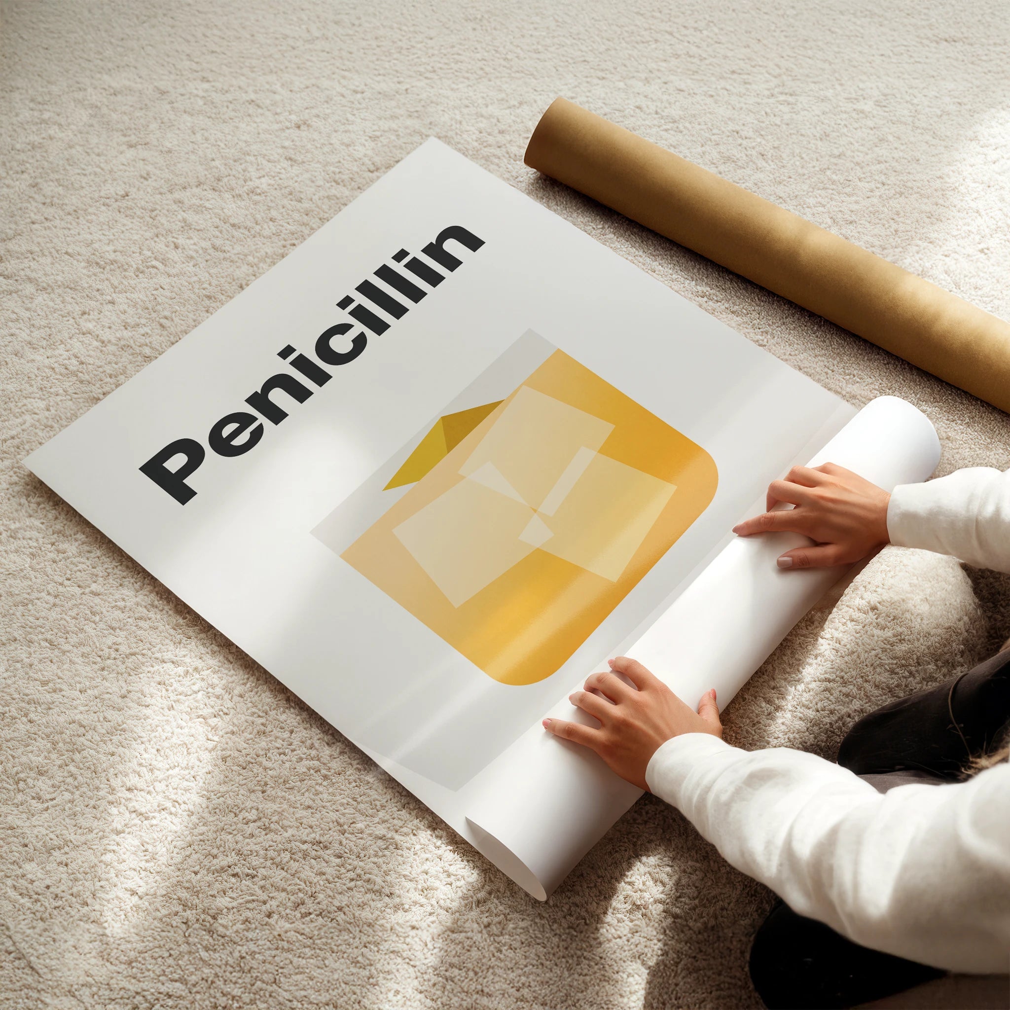 Person unrolling a poster with 'Penicillin' and a yellow capsule on a beige carpet.