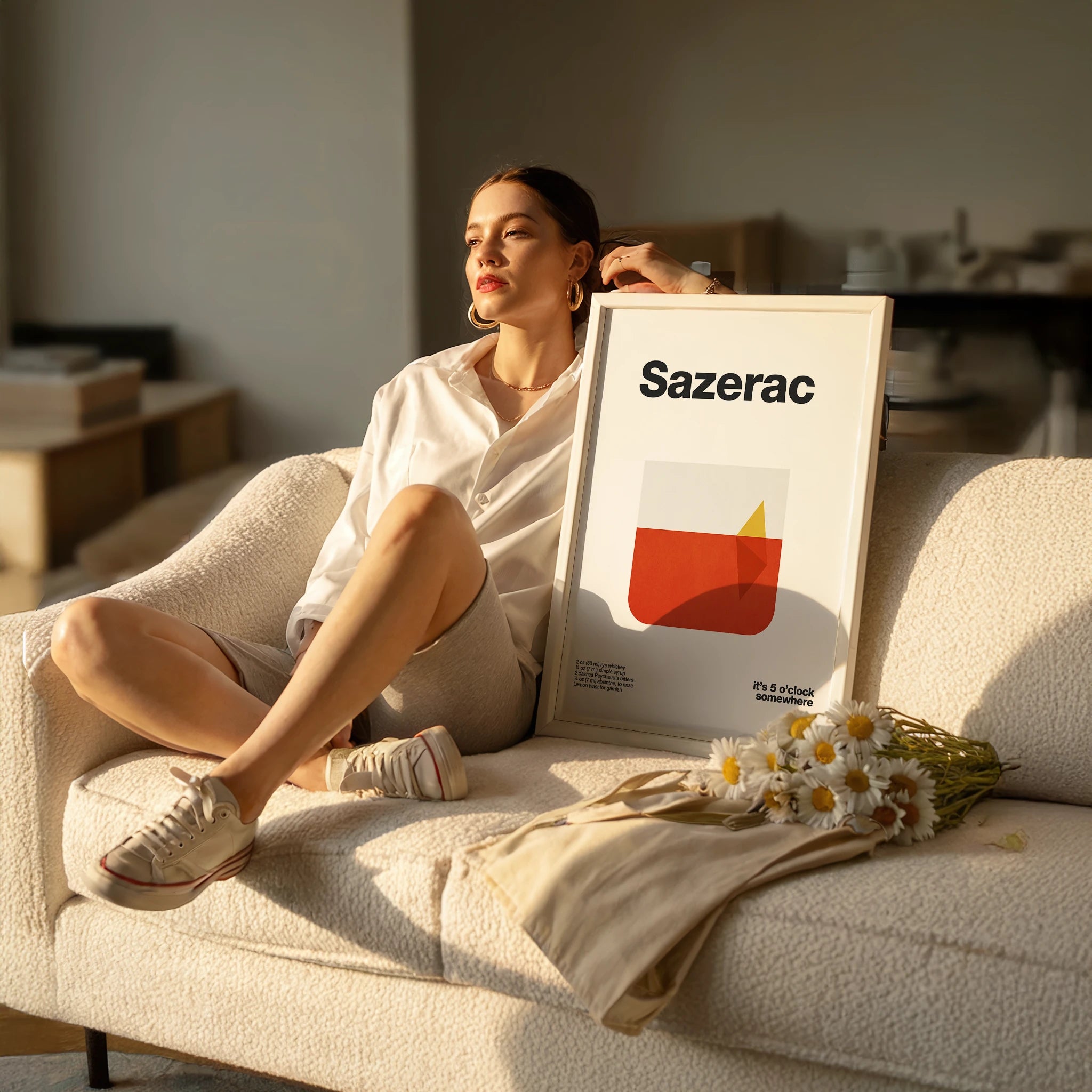 Woman sitting on a couch with a 'Sazerac' poster and flowers