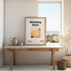 Framed poster with 'Whiskey Sour' design on a wooden table by a window.