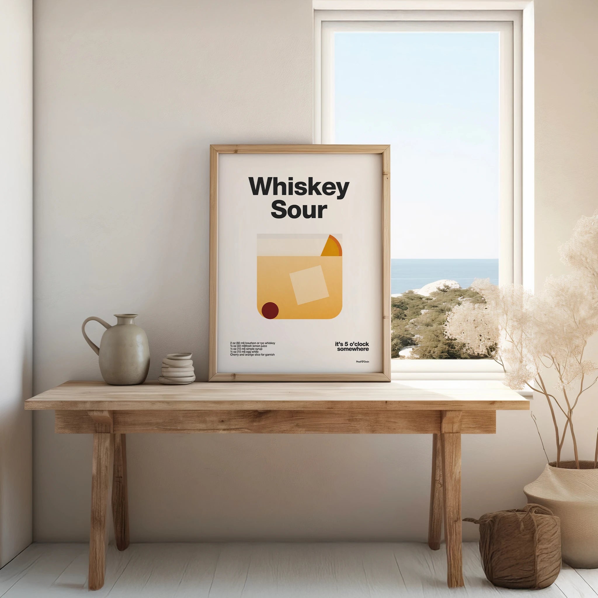 Framed poster with 'Whiskey Sour' design on a wooden table by a window.